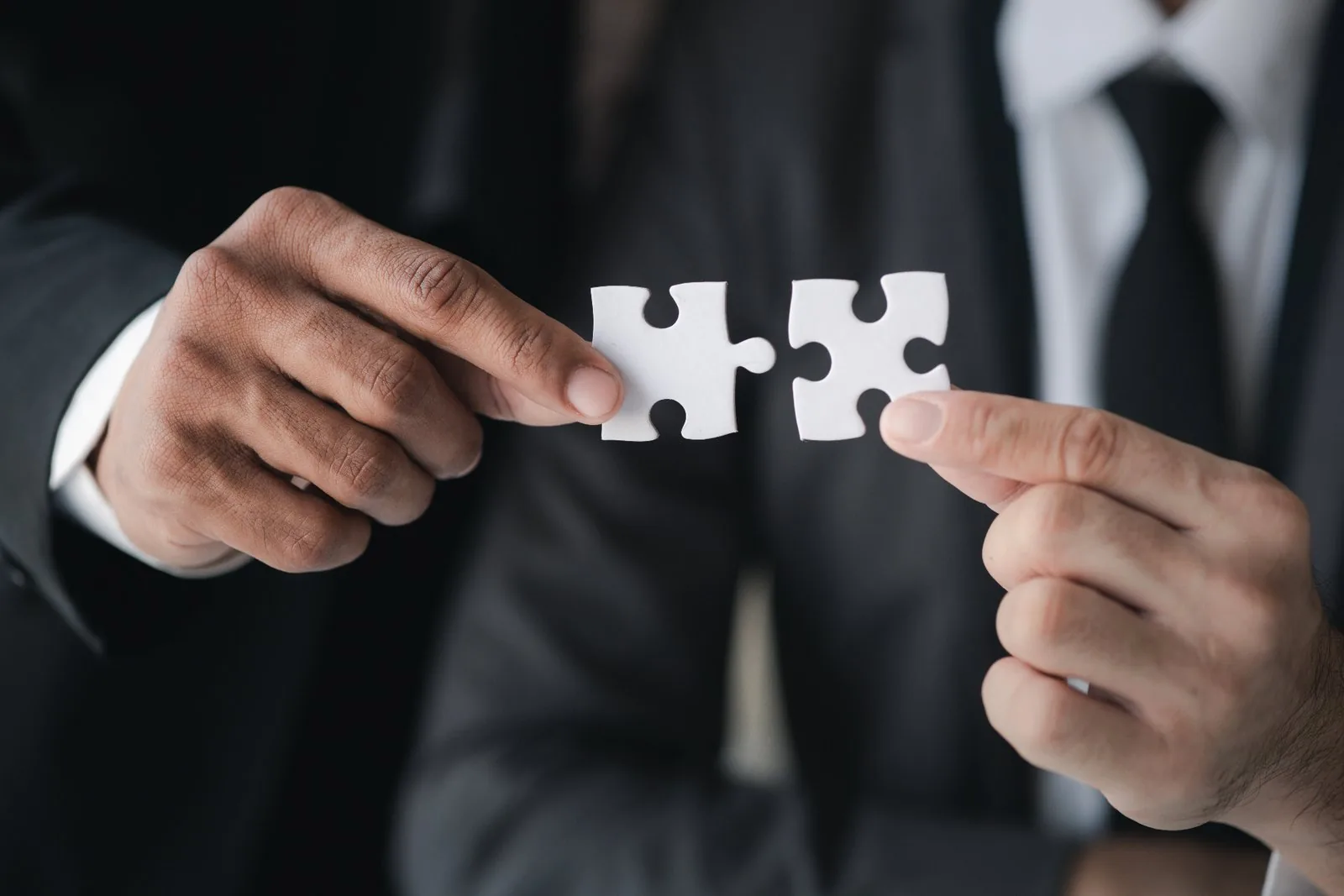 Two professionals connecting puzzle pieces representing corporate partnerships and strategy